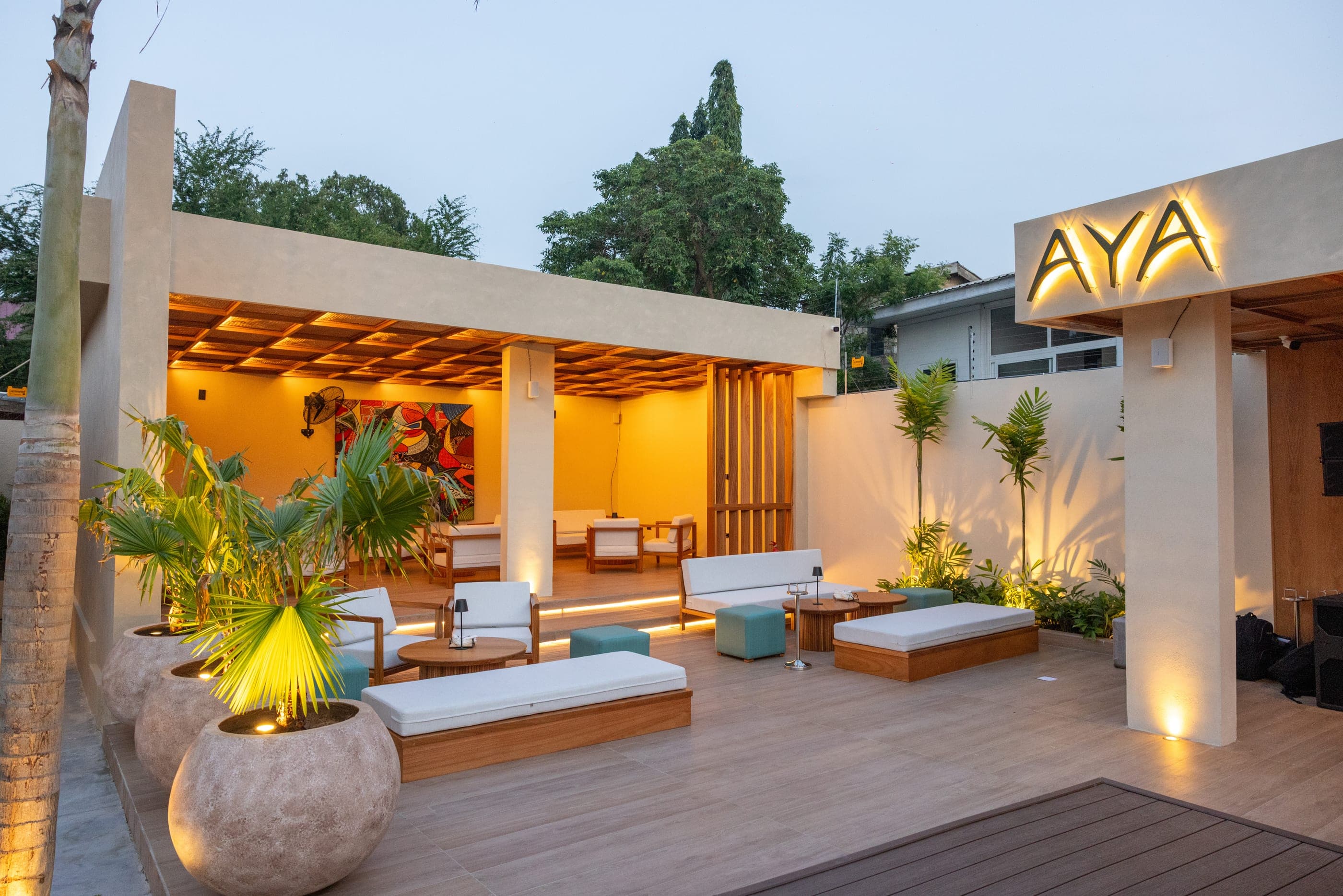 The AYA Restaurant entrance at dusk, the illuminated fern sign on a pale concrete wall above the cabana deck