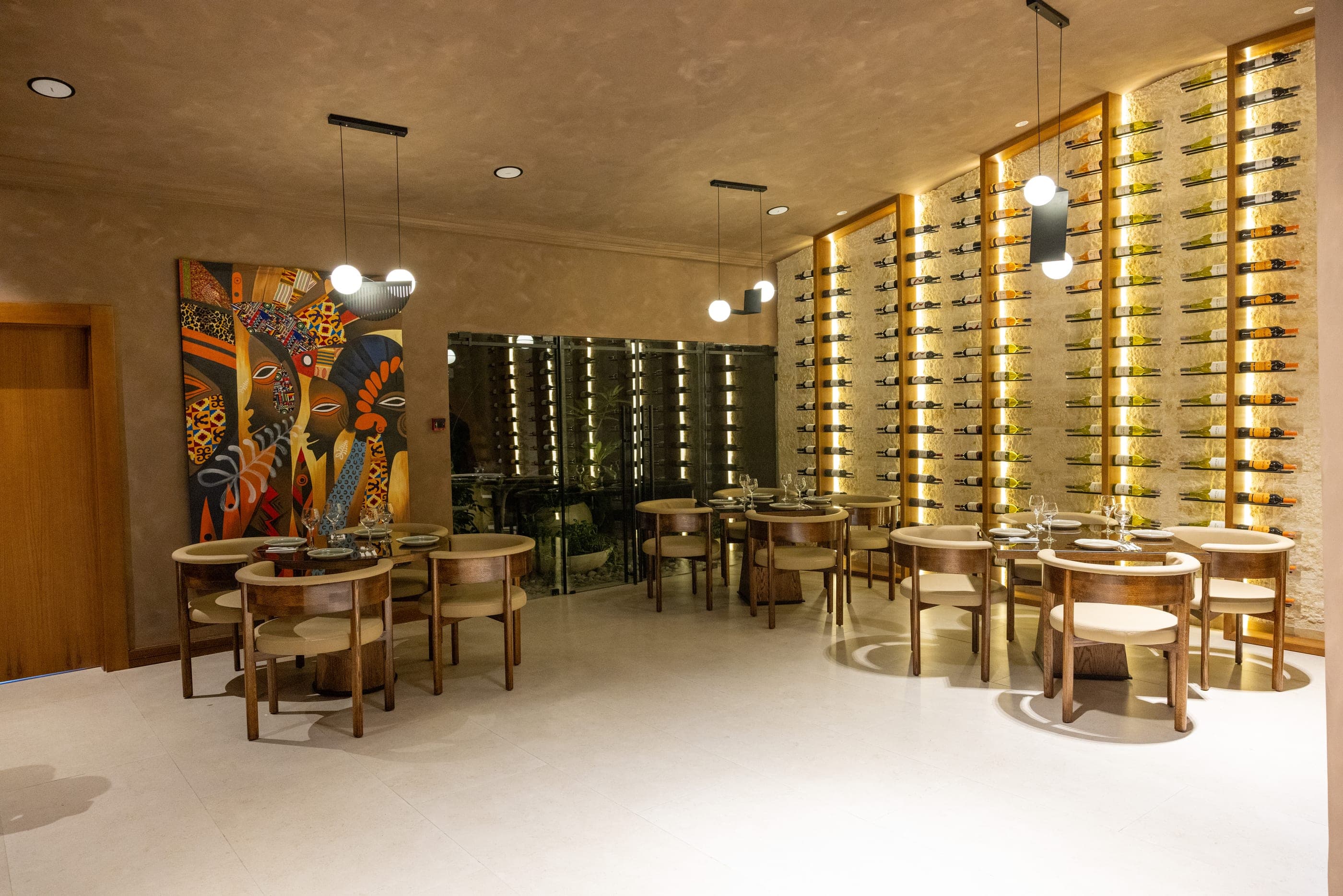 The dining room, round tables under pendant lights beside a floor-to-ceiling wine wall and a large contemporary painting