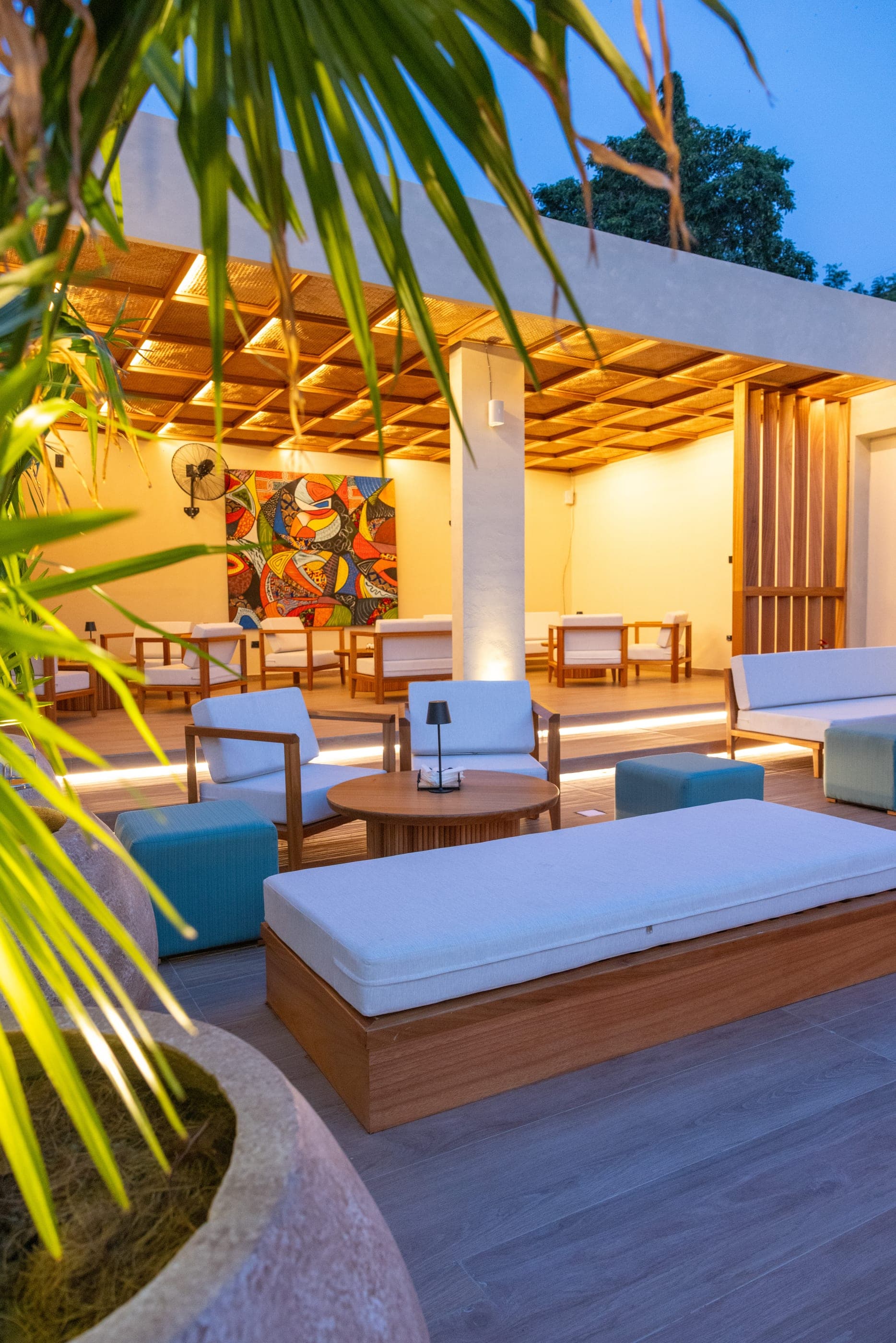 A covered lounge with low seating and a large contemporary painting on the far wall