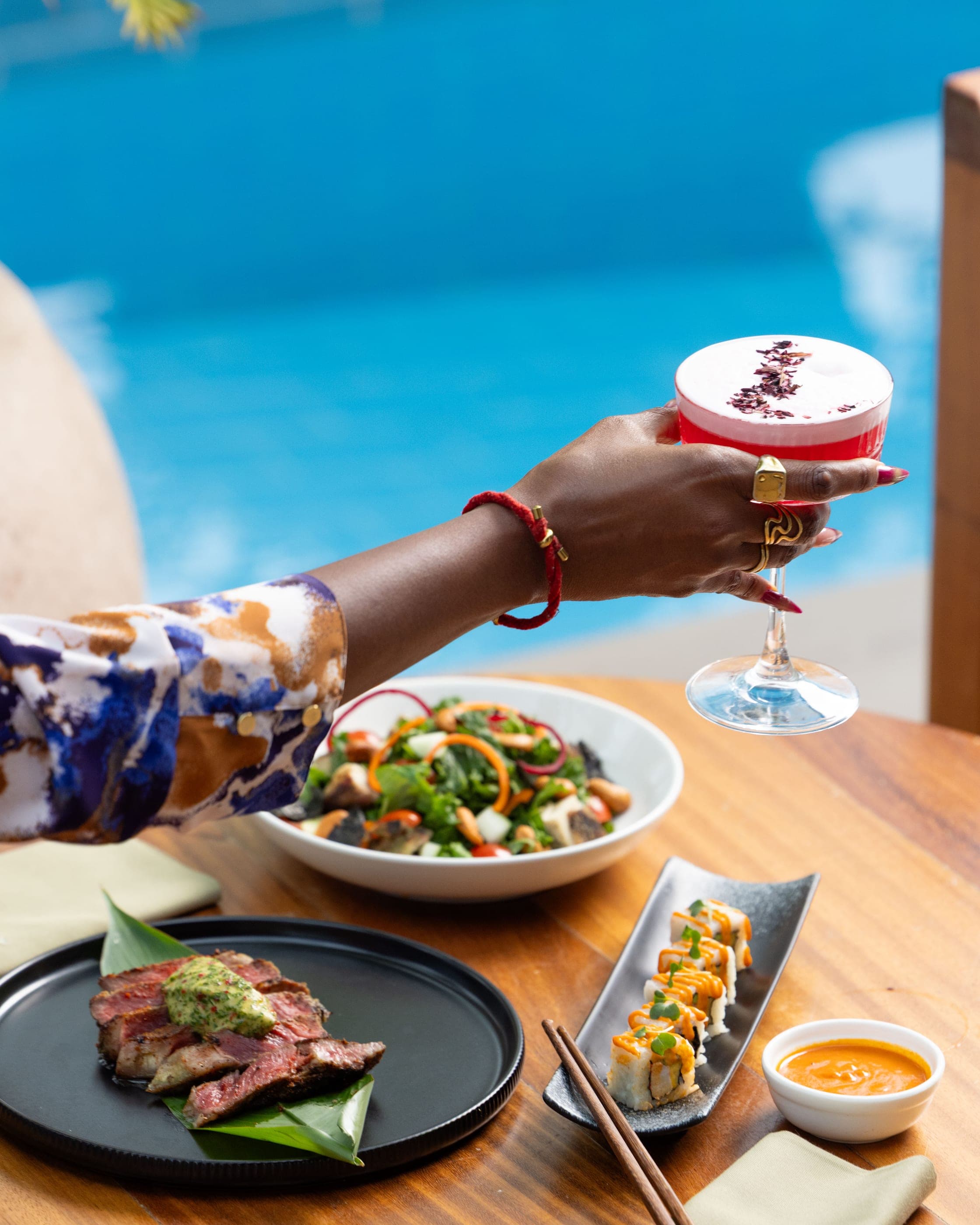 A cocktail being poured into a coupe beside a bowl of salad