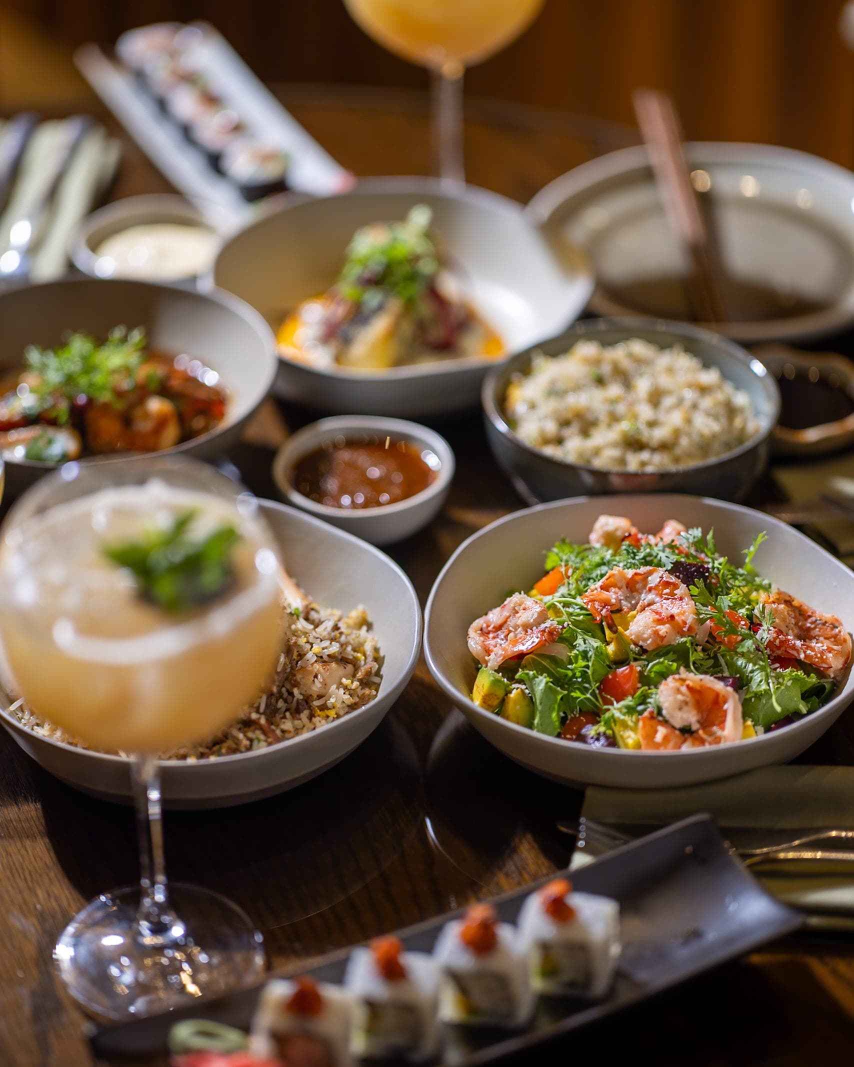 A table of shared dishes and a cocktail, seen from above