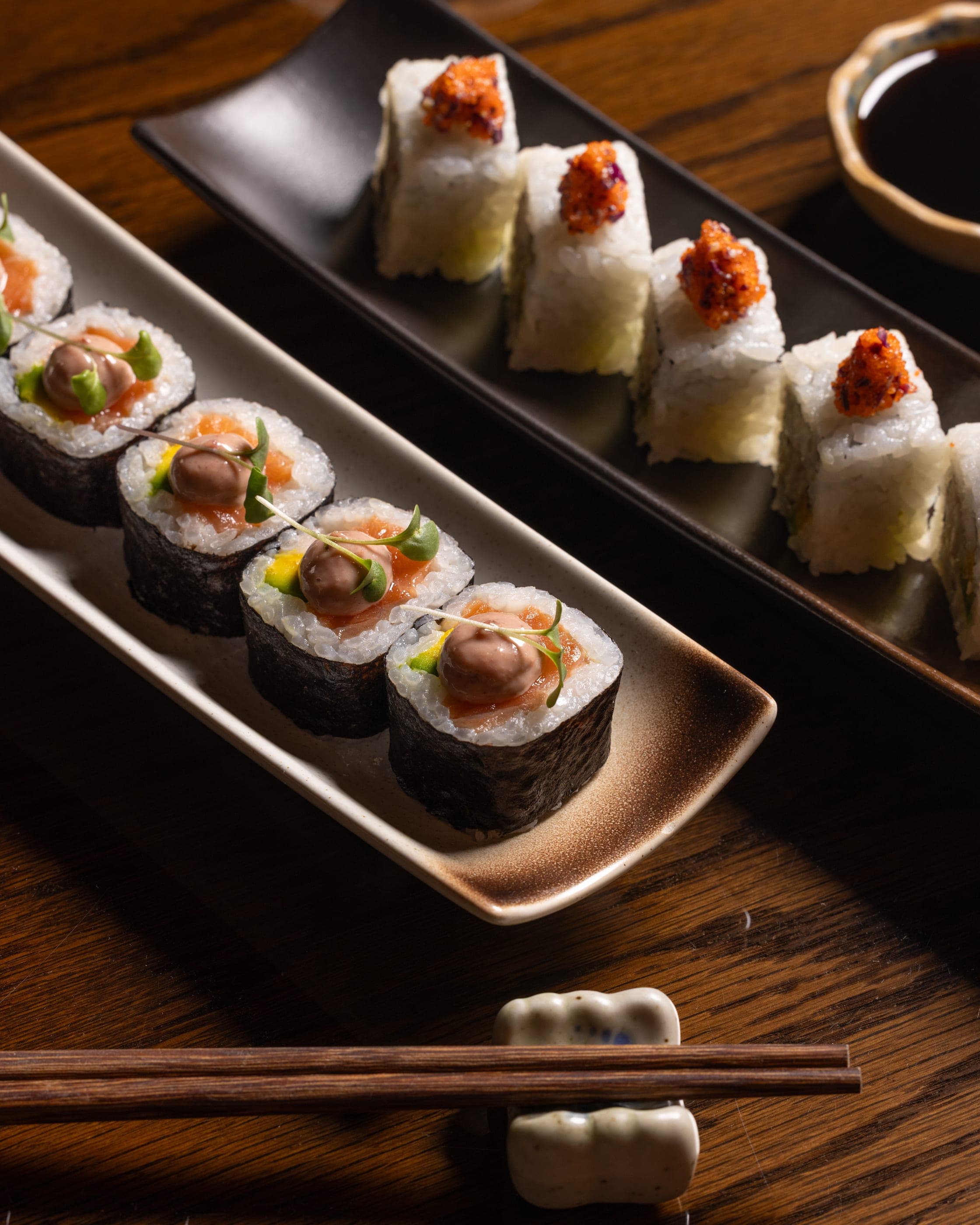 A row of sushi rolls along a dark rectangular plate